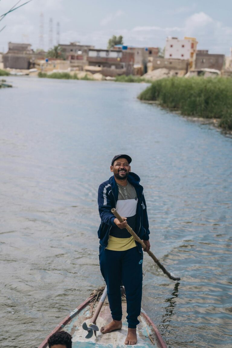 Man happily rowing on a river in Kafr El-Shaikh, Egypt, showcasing local life and scenic views.