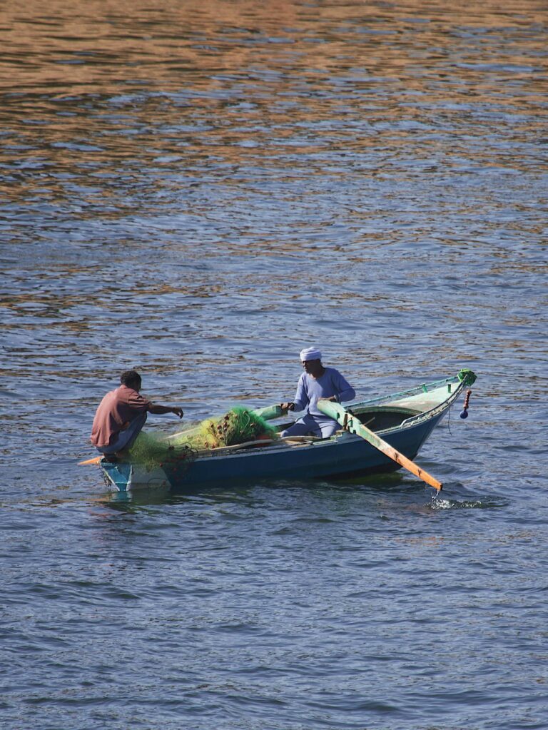 Two fishermen in a boat tending to fishing nets on the Nile River in Egypt.